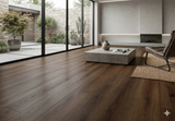 Dark Roast Walnut SPC vinyl plank floor in a bright living room with a stone coffee table and glass doors