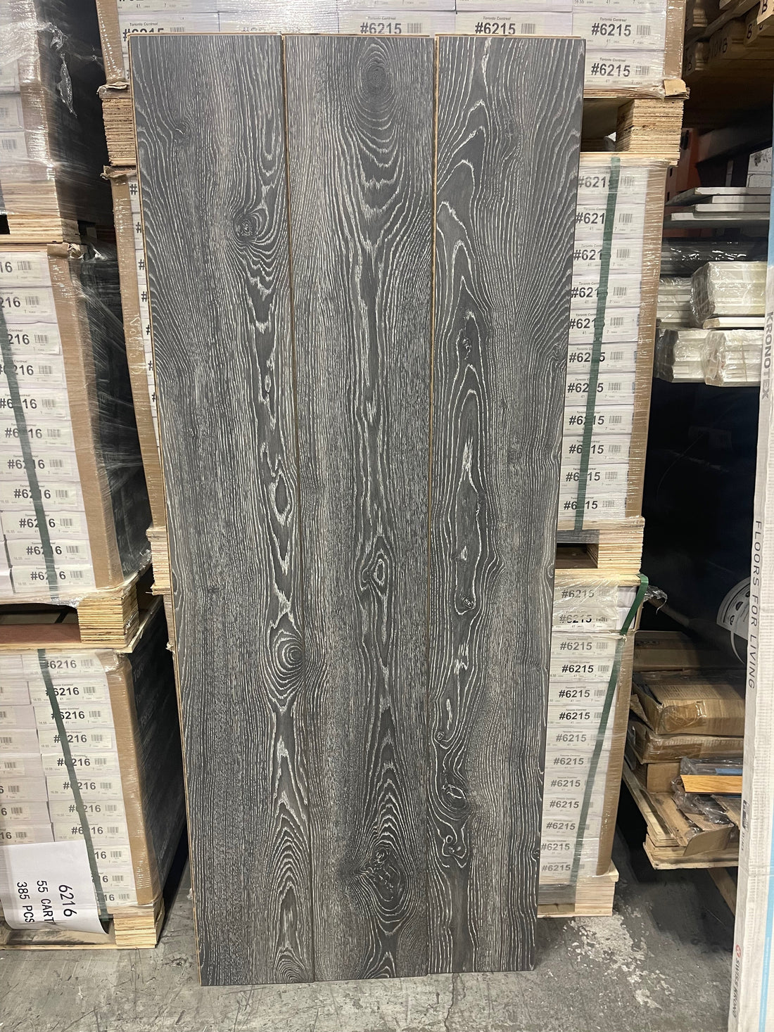 Three Kronotex 4798 laminate planks standing upright, showing a dark grey oak-look grain with pale highlights